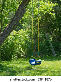 A child's swing sits empty in the backyard in the partial shade on a very hot day.