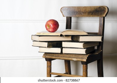 Child's Vintage School Chair Supporting Old Books And Apple. Education Concept.