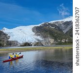 Chile, Patagonia. Kayakers enter the glacier lagoon. Far away on the  path that circles the lagoon, others tourists approach the glacier Aguila on foot located in the Seno de Agostini.