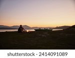 Chile- talca- maule river- woman sitting at camp fire beside canoe