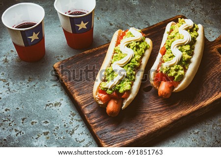 Chilean Completo Italiano. Hot dog sandwiches with tomato, avocado and mayonnaise served on wooden board with drink in paper cup . Top view. Independence Day concept.