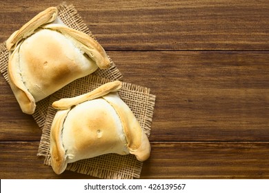 Chilean Empanada, A Baked Pastry Stuffed With Meat, Photographed Overhead On Dark Wood With Natural Light