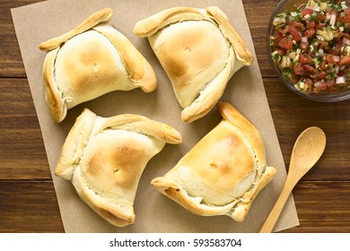 Chilean Empanada, A Baked Pastry Stuffed With Meat, With Chilean Pebre Sauce On The Side, Photographed Overhead On Dark Wood With Natural Light