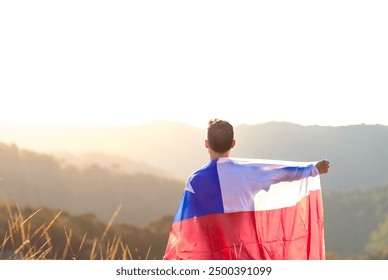 Chilean man with the Chilean flag on his back and arm raised to express national pride and celebration of Chile's Independence Day. In the background, there is a sunset in the mountains. - Powered by Shutterstock