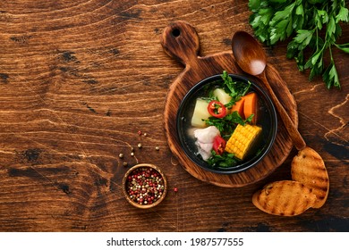 Sopa de carnes chilena con palmitos, maíz, cilantro fresco y papas sobre un fondo de mesa de madera. Cazuela. Comida latinoamericana. 