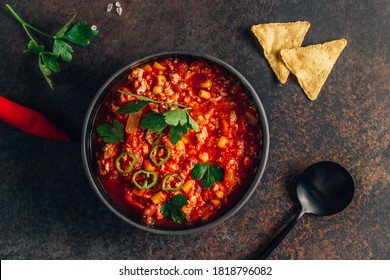 Chili Con Carne in bowl with tortilla chips on dark background. Mexican cuisine. Top view