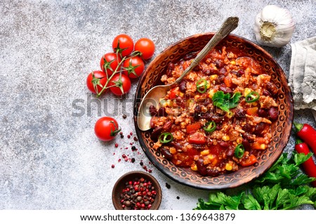 Chili con carne - minced meat stew with red bean and tomato in a clay bowl on a light grey slate, stone or concrete background.Traditional dish of mexican cuisine.Top view with copy space.