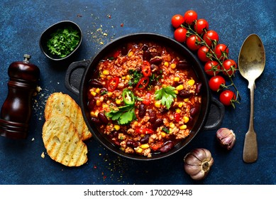 Chili con carne - traditional mexican minced meat and vegetables stew in tomato sauce in a cast iron pan on a dark blue slate, stone or concrete background. Top view with copy space. - Shutterstock ID 1702029448