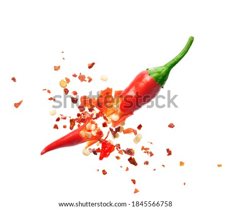 Chili flakes bursting out from red chili pepper over white background
