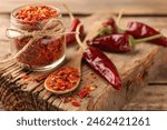 Chili pepper flakes and pods on wooden table, closeup