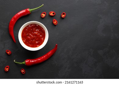 Chili Sauce In A Bowl Along With Chilli Peppers On A Dark Slate Surface With Copy Space. Top View