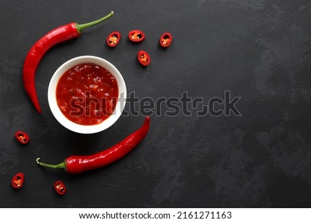 Chili sauce in a bowl along with chilli peppers on a dark slate surface with copy space. Top view