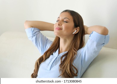 Chill Out Relax At Home. Blissful Young Woman Sitting Listening To Music With Wireless Earphones On Her Mobile Phone At Home As She Relaxes With Closed Eyes On A Sofa.