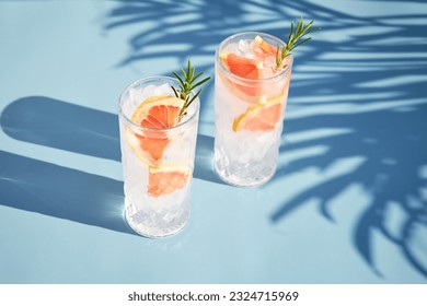 A chilled cocktail with fresh grapefruit slices and a sprig of rosemary under the shade of palm trees. Summer cold drinks. Soda with citrus - Powered by Shutterstock