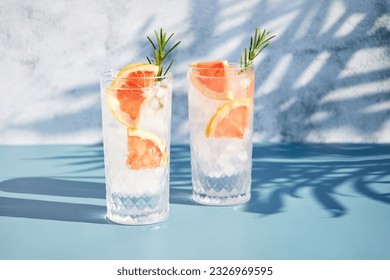 A chilled cocktail with fresh grapefruit slices and a sprig of rosemary under the shade of palm trees. Summer cold drinks. Soda with citrus - Powered by Shutterstock