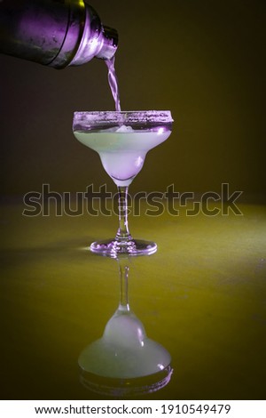 Chilled cocktail mixed with lemon juice and tequilla cointreau poured from the cocktail shaker on the ice cubes in a Margarita glass having salt layer on its rim on Christmas night