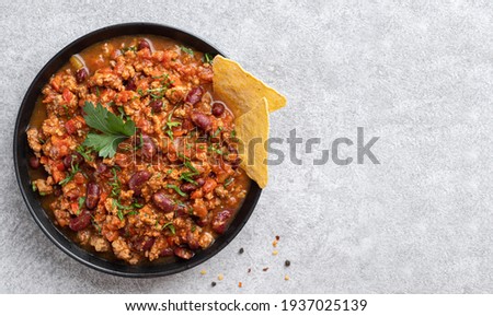 Chilli corn carne in black bowl. Traditional mexican food top view. Stewed minced meat with tomato sauce, red beans and pepper decorated with green parsley leaves and corn nachos chips. Copy space. 
