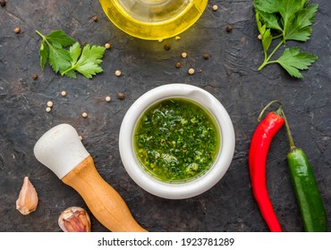 Chimichuri, Argentine green sauce for the steaks with fresh parsley, garlic, olive oil and oregano in a white mortar on a wooden board on a dark concrete background. Sauce recipes. Argentinian cuisine