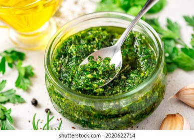 Chimichurri - Latin American sauce made from various herbs, garlic and pepper. Chimichurri verde in a glass bowl on a white background. Sauce of parsley, oregano, rosemary, garlic, pepper, and oil