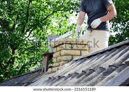 Chimney construction, repairs and re-building. A contractor is bricklaying a brick chimney on an house asbestos roof. 