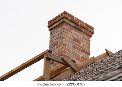 Chimney made of expanded clay block. Tiled with antique red brick. The seams are filled withcement-sand mortar with the addition of calcium.  Aspen wooden roof tiles. Scaffolding. Cloudy gray sky. - Shutterstock ID 2223531605