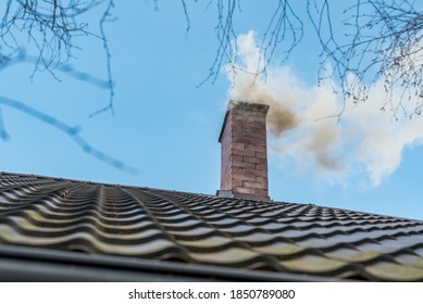 Chimney on the roof of a detached house. The smoke from the chimney. House heating, beginning of the heating season. Burning coal and wood in the furnace. Air pollution and smog in the winter season.