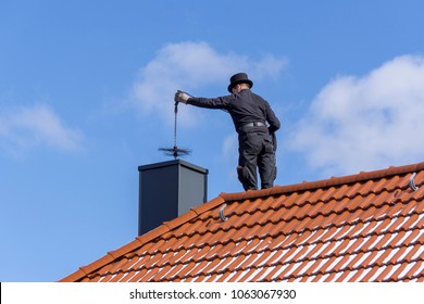 Chimney sweep cleaning a chimney standing on the house roof, lowering equipment down the flue
