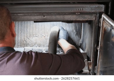 Un deshollinador limpia el interior de un inserto de chimenea con una aspiradora, para mantenimiento y seguridad.