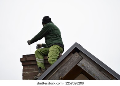 Chimney sweep man cleaning brown brick chimney on building roof on clear sky background with copy space for text.
