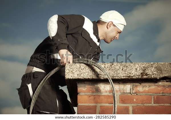 Chimney sweep man in work uniform cleaning chimney\
on building roof