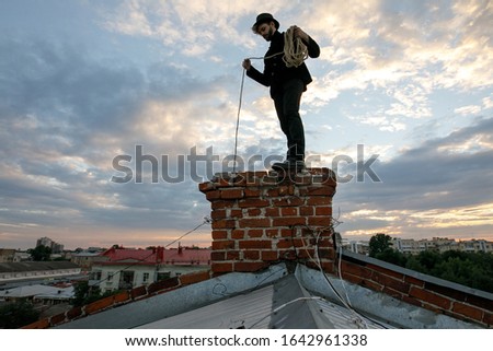 Chimney sweep young man with beard and dirty face on the roof 