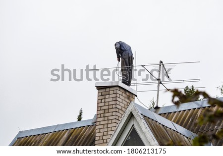 Chimney sweeper clears ash and soot from chimneys on cloudy autumn day.
