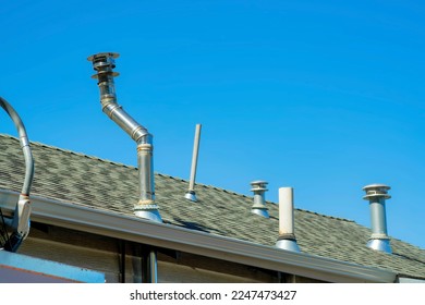 Chimney vents in rows on top of double gable style roof with gray pannels on top of house or home with gradient blue sky. Late in the afternoon sunlight in a suburban part of downtown neighborhood.