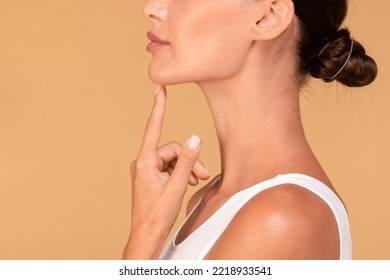 Chin augmentation. Side view of unrecognizable young woman touching her face, happy with result of plastic surgery, beige studio background with free space - Powered by Shutterstock