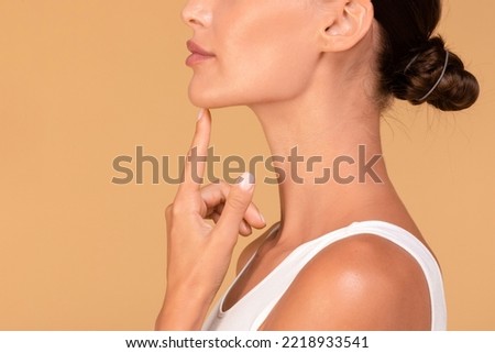 Chin augmentation. Side view of unrecognizable young woman touching her face, happy with result of plastic surgery, beige studio background with free space