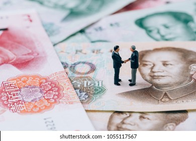 China finance tariff trade war negotiation talk concept, miniature people businessman leader handshaking on Chinese yuan banknotes, world major market countries, import and export barrier.
