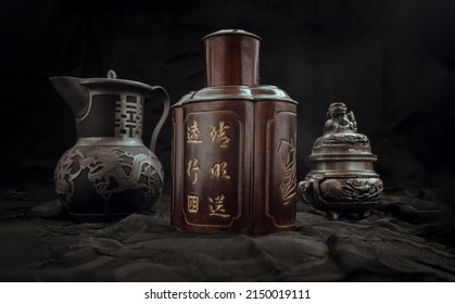 Chinese antique tea leaf iron storage jar (Characters chinese is Name of the tea), Chinese antique teapot (Characters chinese is Double Happiness) and Silver antique incense burner on dark background.