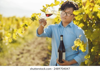 Chinese Appearance Sommelier Tasting Red Wine Through Analysis it Color Standing on Row of Sunlit Vineyards - Powered by Shutterstock