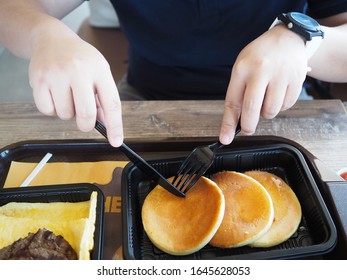 Chinese Asian Guy Who Wear Watch Is Using Plastic Knife And Fork And Cutting Pancake Breakfast Burger King Meal In Bangkok Thailand. February 12,2020