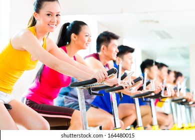 Chinese Asian Sport Group Of Men And Women In Fitness Club Or Gym Exercising On Bikes 