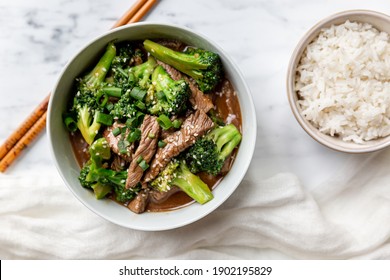 Chinese black pepper beef and broccoli stir-fry served in a light bowl on a light marble surface with bowl of rice and a white cloth, delicious lunch. - Powered by Shutterstock