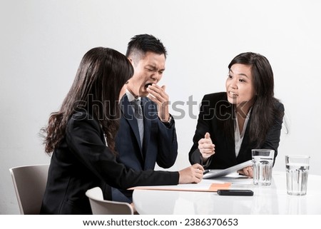 Chinese business man yawning during a business meeting in front of work colleges 