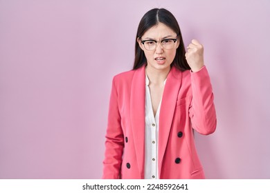 Chinese business young woman wearing glasses angry and mad raising fist frustrated and furious while shouting with anger. rage and aggressive concept.  - Shutterstock ID 2248592641