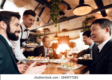 Chinese businessman looks at a man with a beard and smiles. A waiter gives a man in a sushi suit while he is talking with a Chinese businessman.