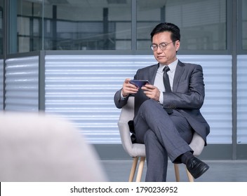 Chinese Businessman In Suit And Tie Using Cellphone To Watch Live Streaming Or Video