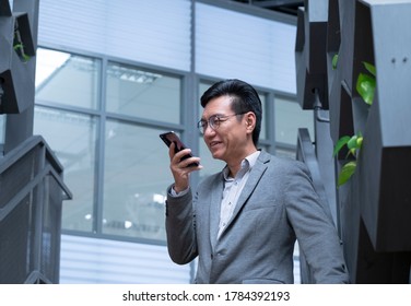 Chinese Businessman Wearing A Jacket, Smiling And Using His Cellphone To Leave A Voice Message