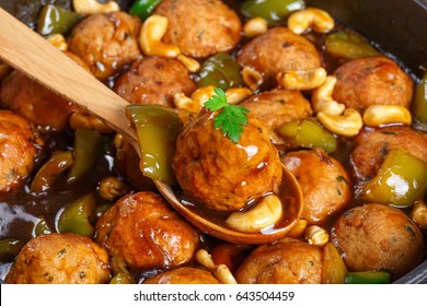 Chinese Cashew Chicken Meatballs Tossed With Sauce Of Green Bell Pepper Chunks, Onion, Soy Sauce, Chinese Cooking Wine And Spices In Pan And  One Meatball On Wooden Spoon, Close-up, Selective Focus