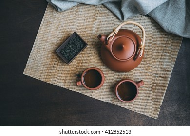 Chinese Ceremony.  Brown Ceramic Pot And Brown Cup. Green Tea On Bamboo Mat And Aged Wooden Table. Top View.