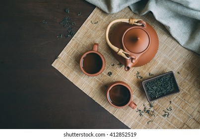 Chinese Ceremony.  Brown Ceramic Pot And Brown Cup .Green Tea On Bamboo Mat & Aged Wooden Table. Top View.