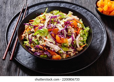 Chinese Chicken Salad with shredded chicken meat, mandarin oranges, crunchy noodles, red cabbage, napa cabbage, carrots, green onions in bowl